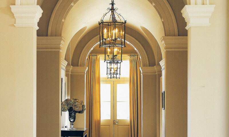 Elegant hallway with chandelier and arched-doorway.